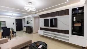 A modern living room with a flat-screen TV, a sofa, a coffee table, and a dining area with chairs and a table. - Ocean Apartments (Cairo)