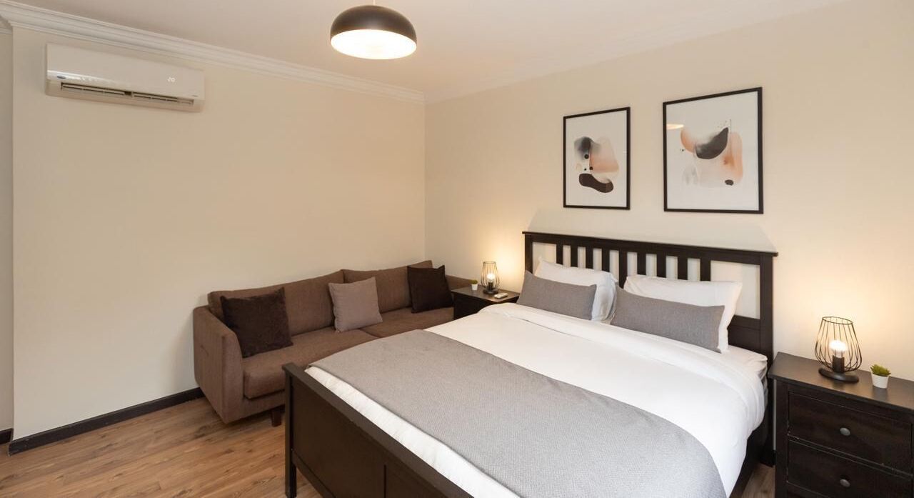 Een slaapkamer met een bed, een bank, een nachtkastje met een lamp en twee ingekaderde foto's aan de muur.