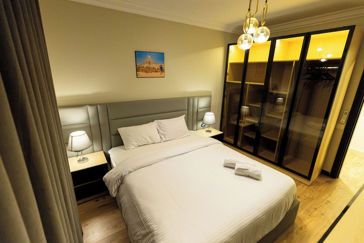 A hotel room with a large bed, two bedside tables with lamps, a wardrobe with a mirror, and a picture on the wall.
