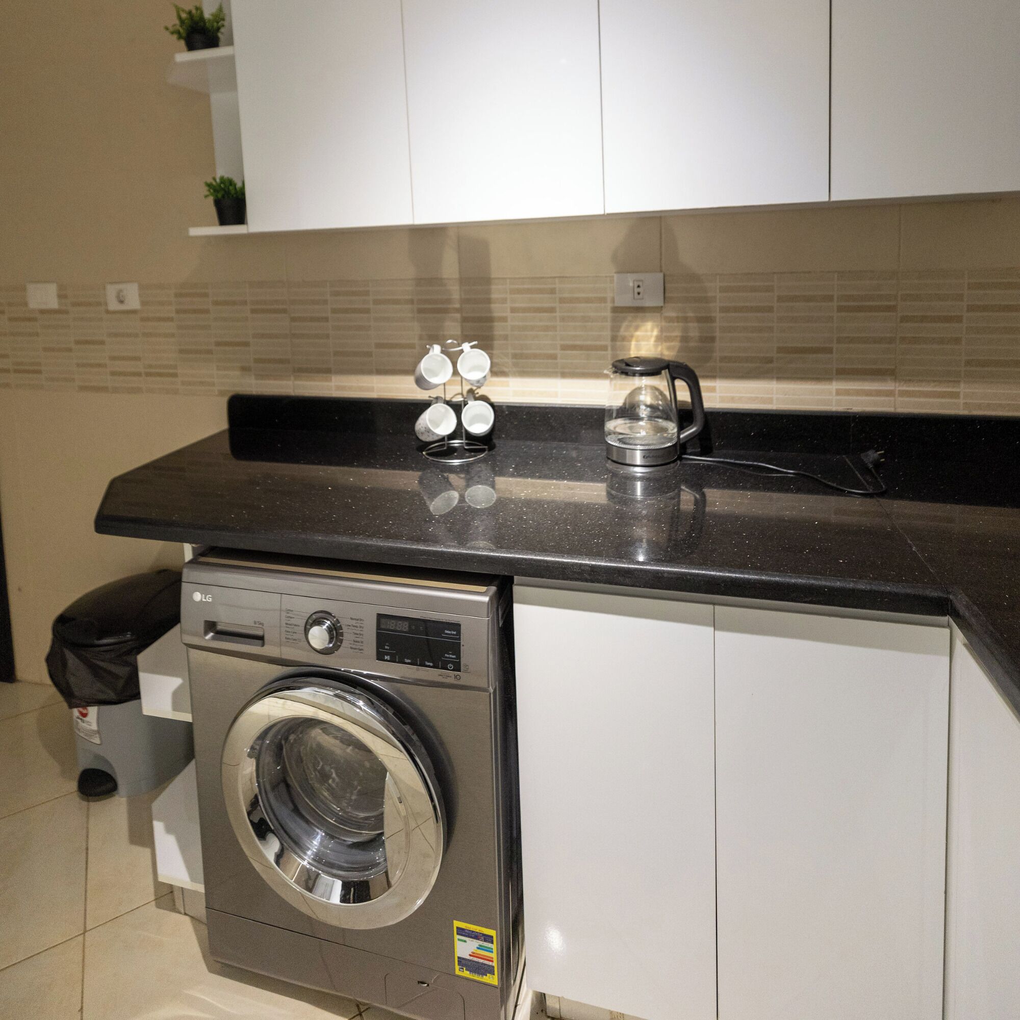 A compact kitchen with a built-in washer and dryer, a coffee maker, and a small plant on the countertop.