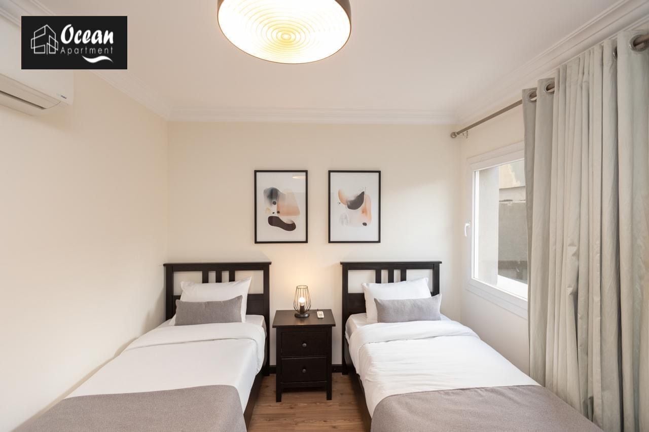 Ein Hotelzimmer mit zwei Betten, einem Nachttisch mit Lampe und zwei gerahmten Bildern an der Wand.