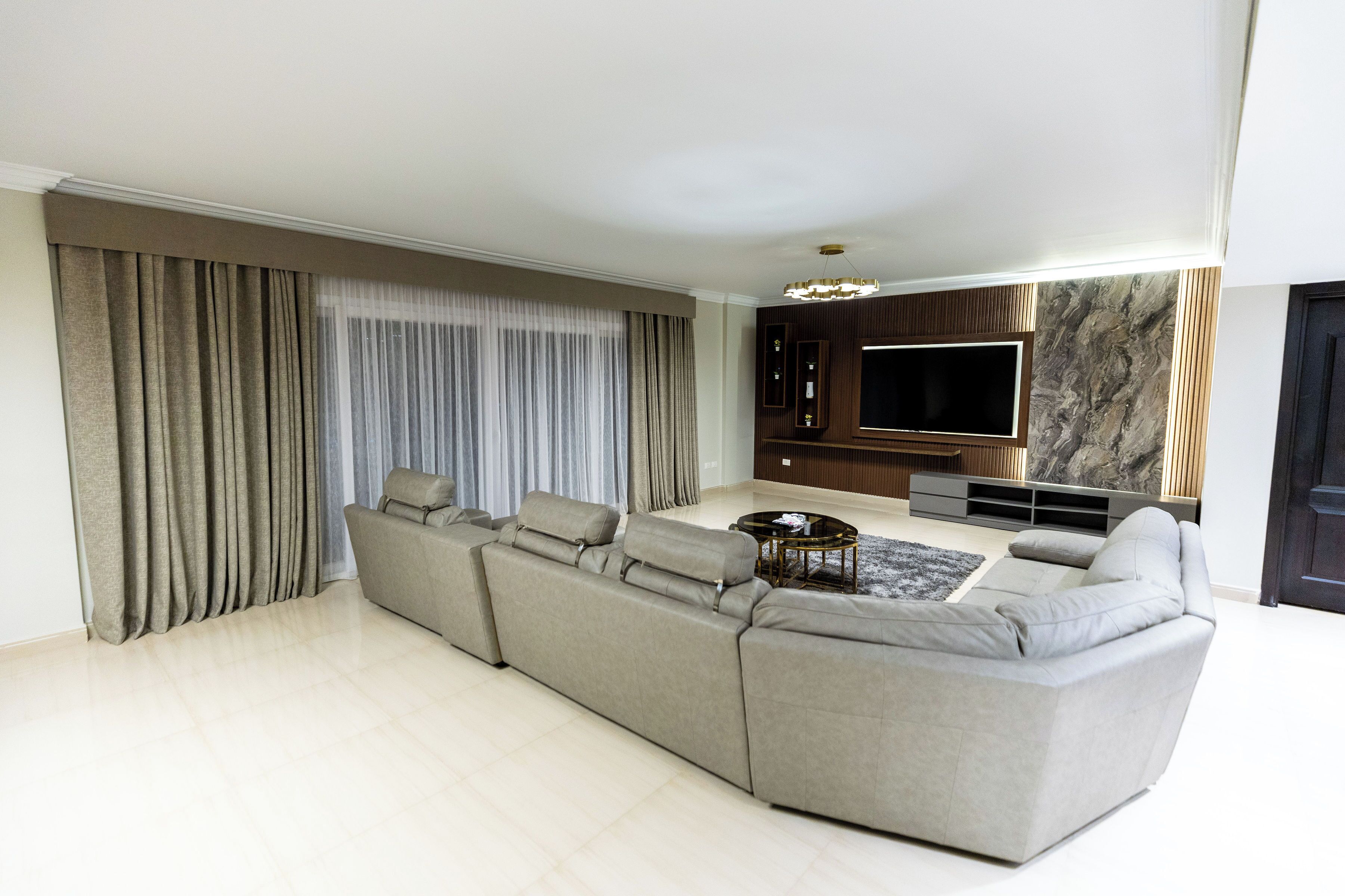 A modern living room with a large sectional sofa, a flat-screen TV, and a marble accent wall.
