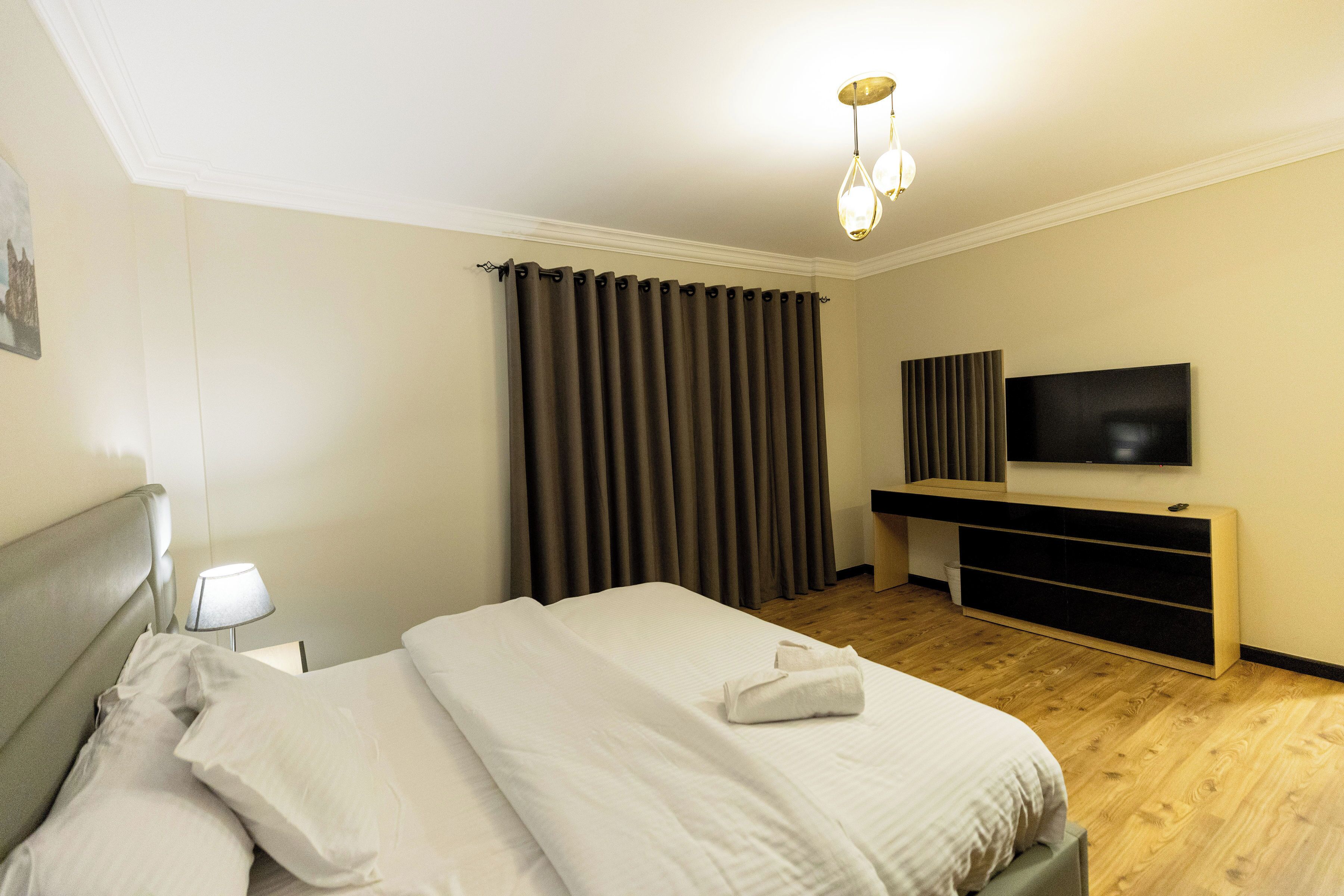 A hotel room with a bed, a TV, a desk, and a window with curtains.