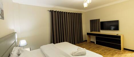 A hotel room with a bed, a TV, a desk, and a window with curtains.