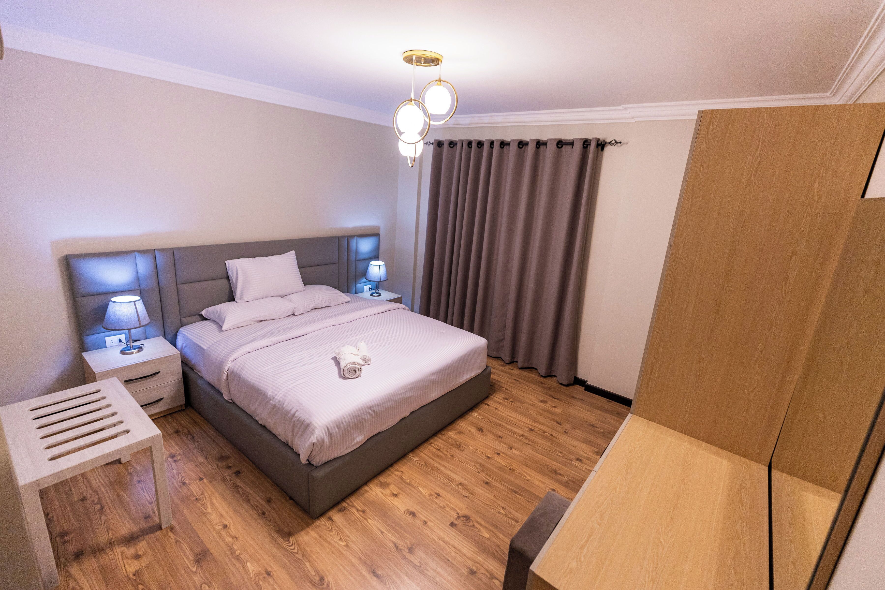 Een moderne slaapkamer met een groot bed, nachtkastjes, een nachttafeltje, een houten vloer en een plafondlamp.