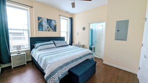 Un dormitorio con cama, ventilador de techo, ventana con cortinas, una puerta y lámpara fijada a la pared.