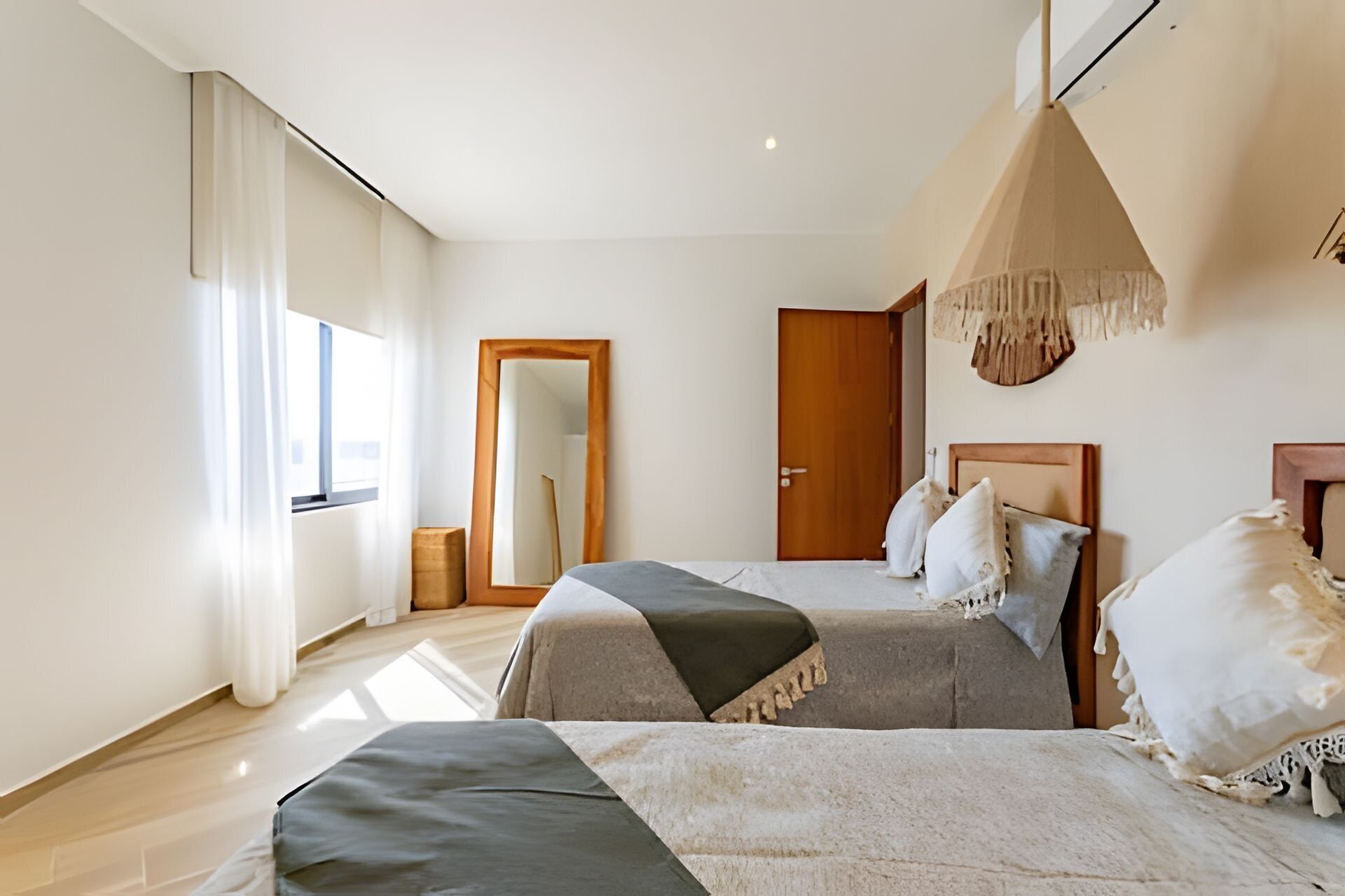 A modern bedroom with two beds, a large mirror, a wooden door, and a hanging light fixture.