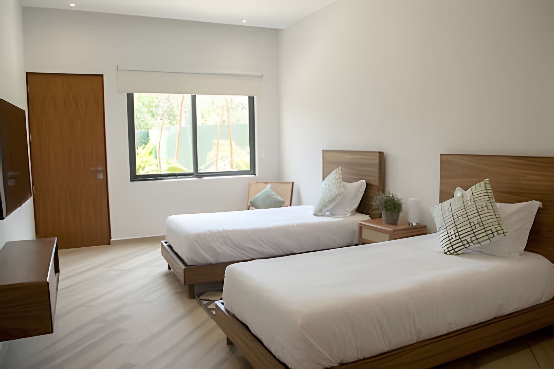 A hotel room with two beds, a TV, and a window with a view of greenery.