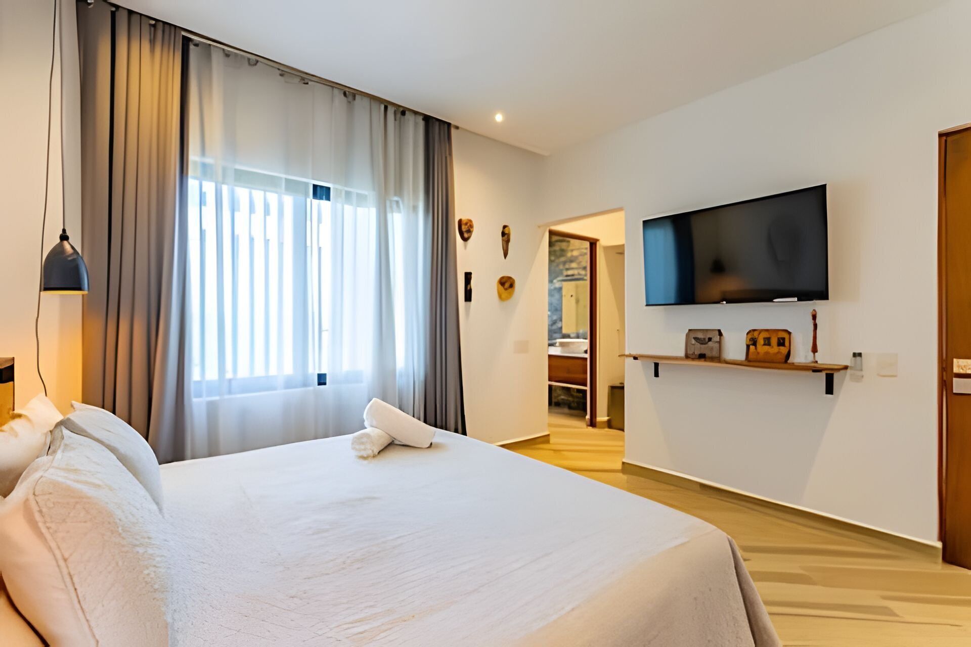 A hotel room with a bed, a TV mounted on the wall, and a window with curtains.