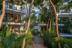 A modern building with multiple balconies, surrounded by lush greenery and a pathway leading to the entrance.