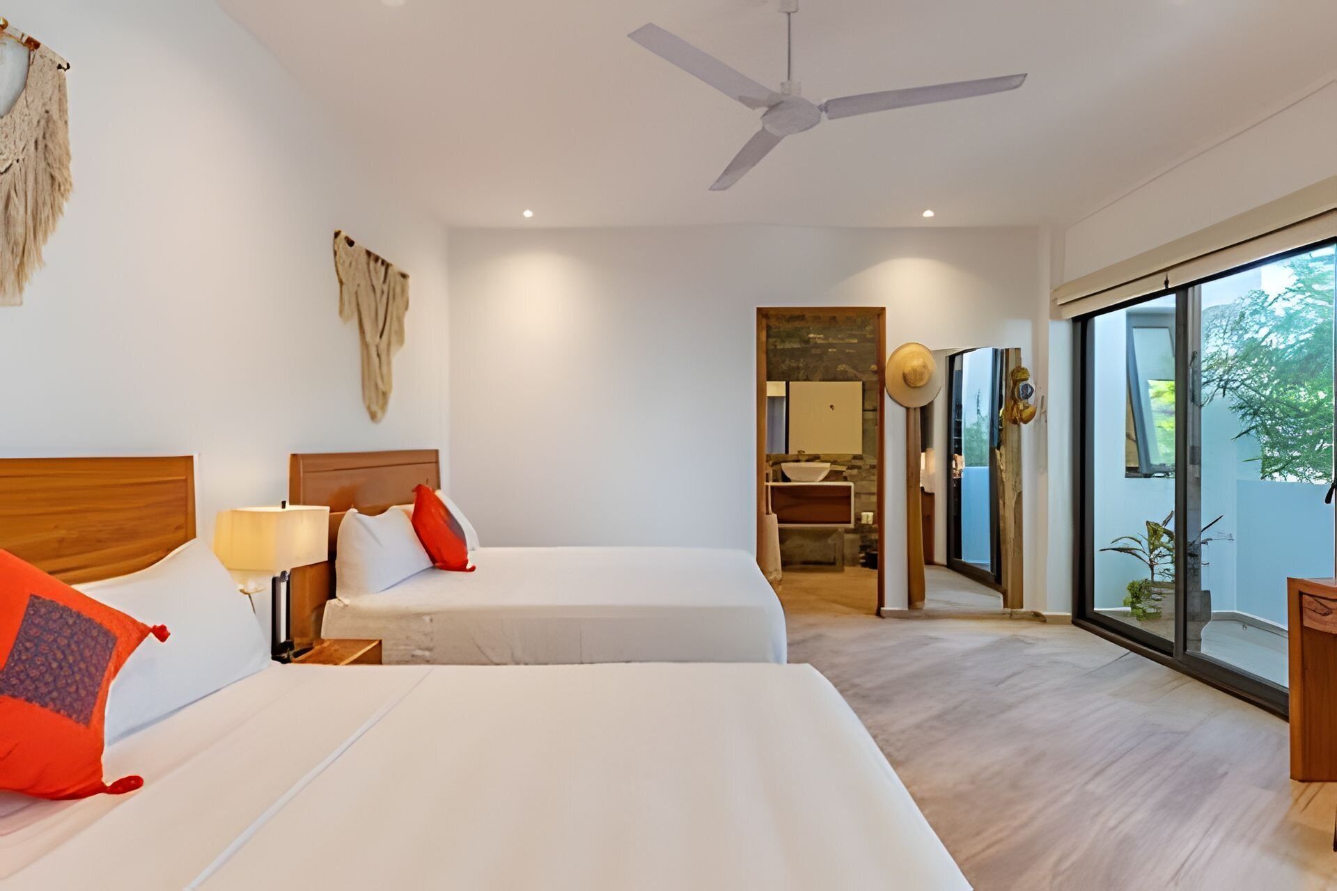 A hotel room with two beds, a ceiling fan, a large window, and a view of the outdoors.