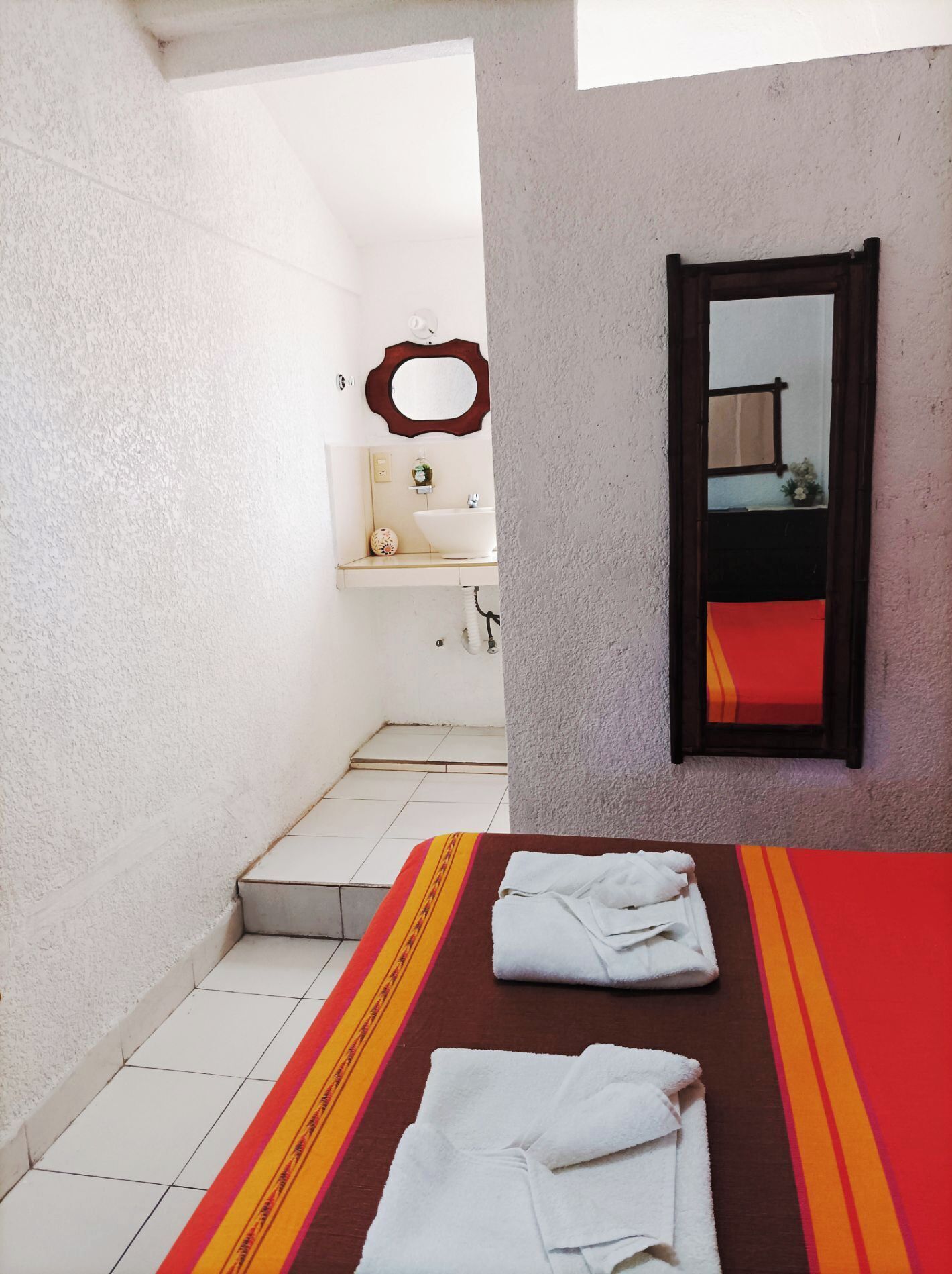 A small bathroom with a white sink, a mirror, and a red and yellow striped towel on the floor.