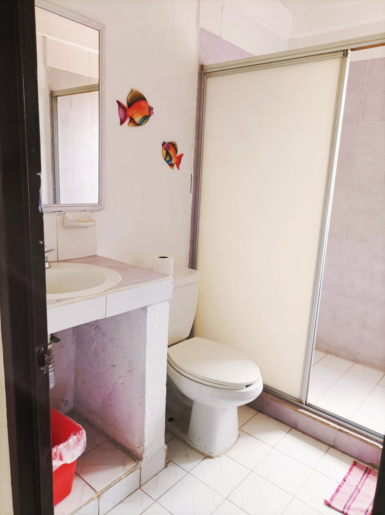 A bathroom with a white sink, toilet, and shower area. There are two fish decorations on the wall.