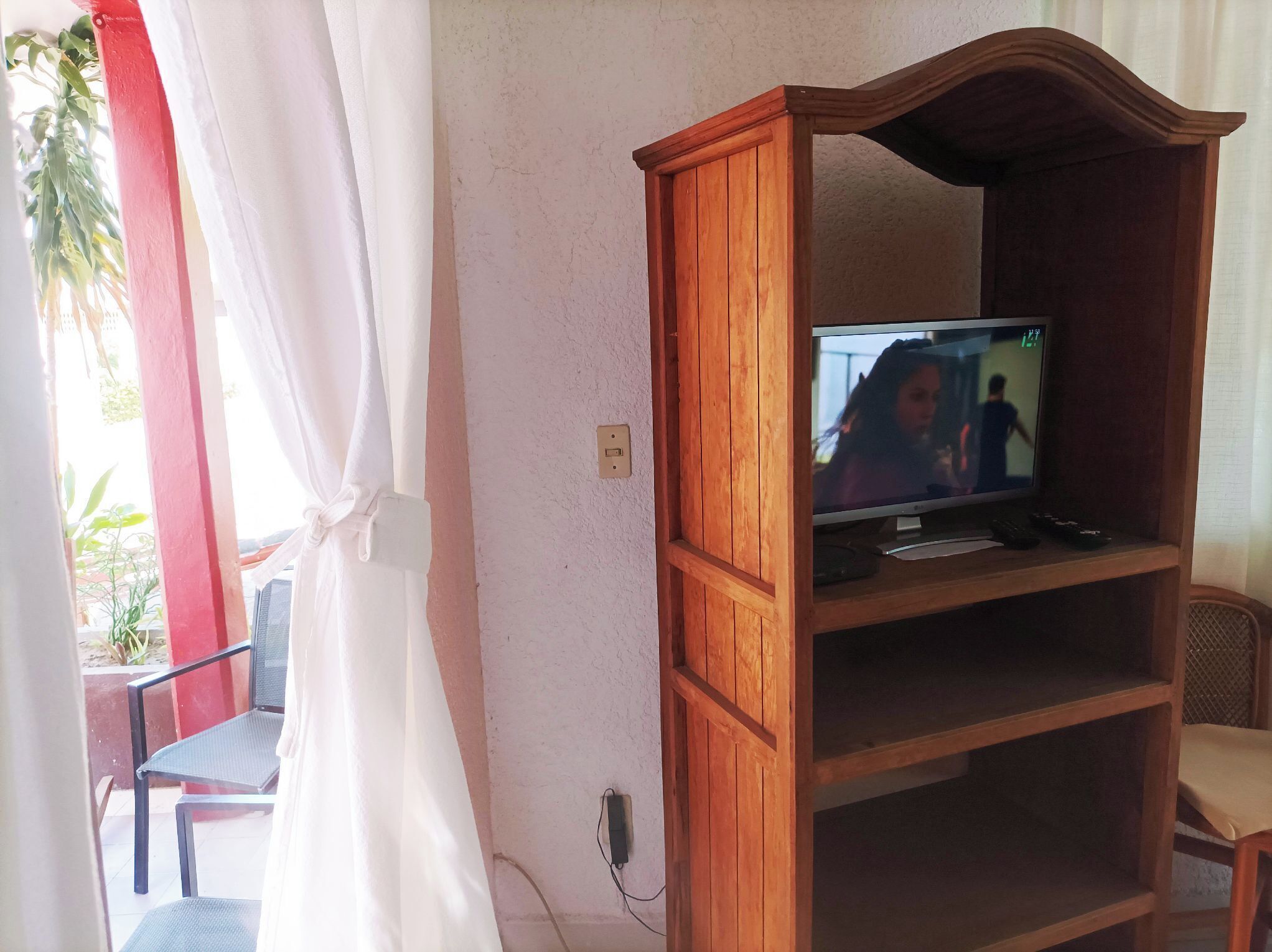 Un meuble de rangement en bois comprenant un téléviseur, une prise de courant et une chaise.