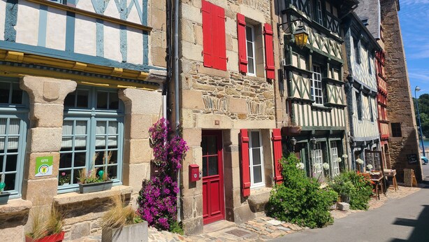 Ein traditionelles europäisches Gebäude mit steinverkleideter Fassade, Fachwerk und roten Fensterläden.