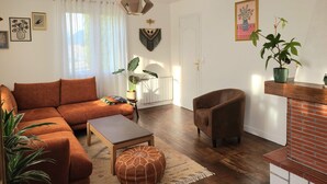 Ein Wohnzimmer mit Sofa, Sessel, Couchtisch und Zimmerpflanzen.