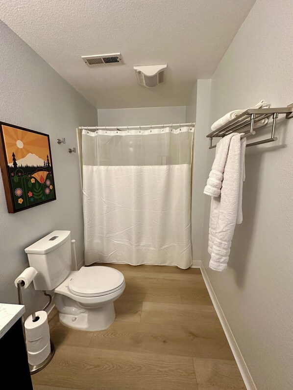 A bathroom with a toilet, a shower curtain, a towel rack, and a painting on the wall. - Cozy studio that sleeps 4 in Kenmore with a/c, WiFi and farm fresh eggs! (Kenmore)