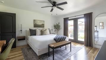 Un dormitorio moderno con una cama grande, un ventilador de techo, un banco, una mesita de noche, una silla y vistas al exterior.