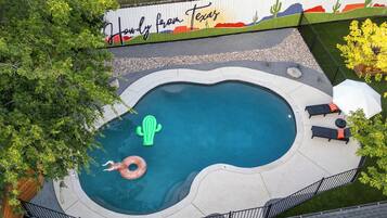 Una piscina de forma singular, rodeada por una valla blanca con un mural, y equipada con sillas de descanso y una sombrilla.