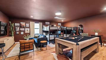 A cozy living area with a pool table, a sofa, a coffee table, and a bookshelf.