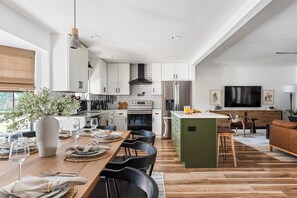 A modern kitchen with white cabinets, a central island, and a dining area with a wooden table and chairs. - IG-Worthy TX Oasis: Gated Pool + Fire Pit + Putt Putt + Game Room (North Richland Hills)