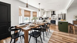 Eine moderne Küche mit Essbereich, ausgestattet mit einem Holztisch, schwarzen Stühlen und Pendelleuchten.