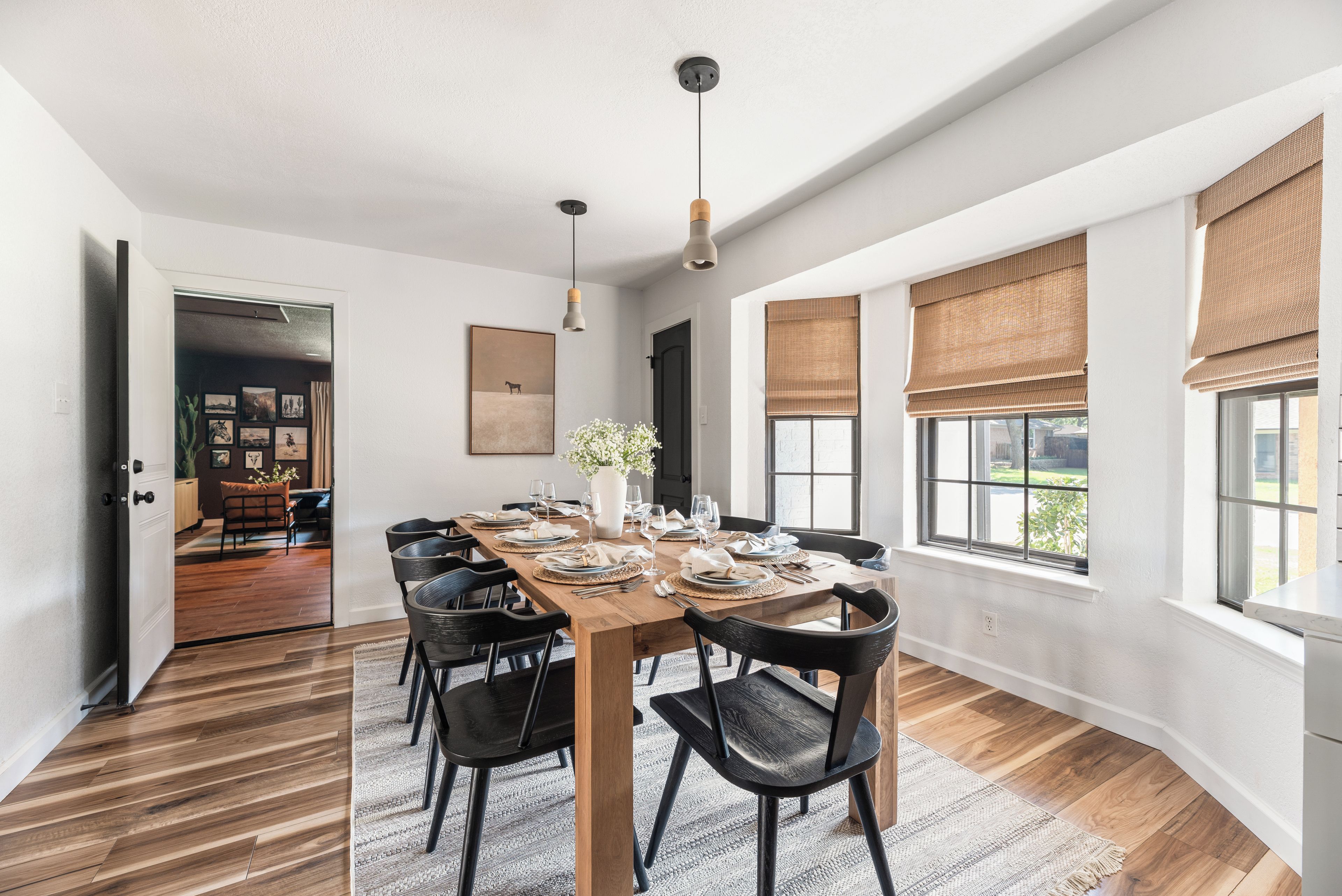 Comedor con una mesa de madera dispuesta para seis personas, rodeada de sillas negras, con ventanas amplias y vistas al exterior.