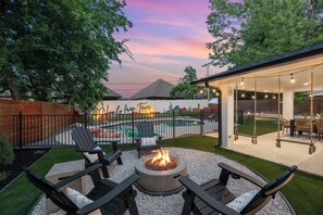 Ein Garten mit Feuerstelle, Sitzgelegenheiten im Freien, einem Pool und einer überdachten Terrasse.