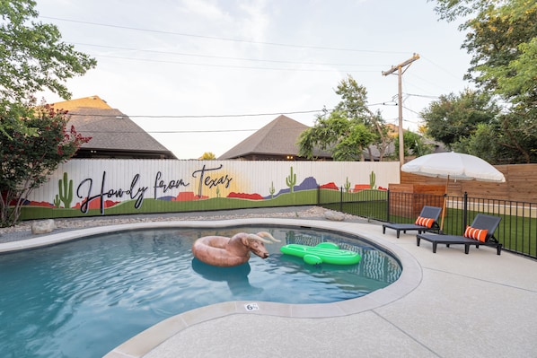 A swimming pool with a mural, lounge chairs, and a cactus decoration.