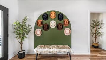 Une pièce avec un mur vert, un banc recouvert d’un plaid en fausse fourrure et un présentoir à chapeaux fixé au mur.
