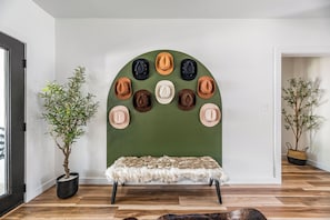 A room with a green wall, a bench with a fur throw, and a wall-mounted hat display.