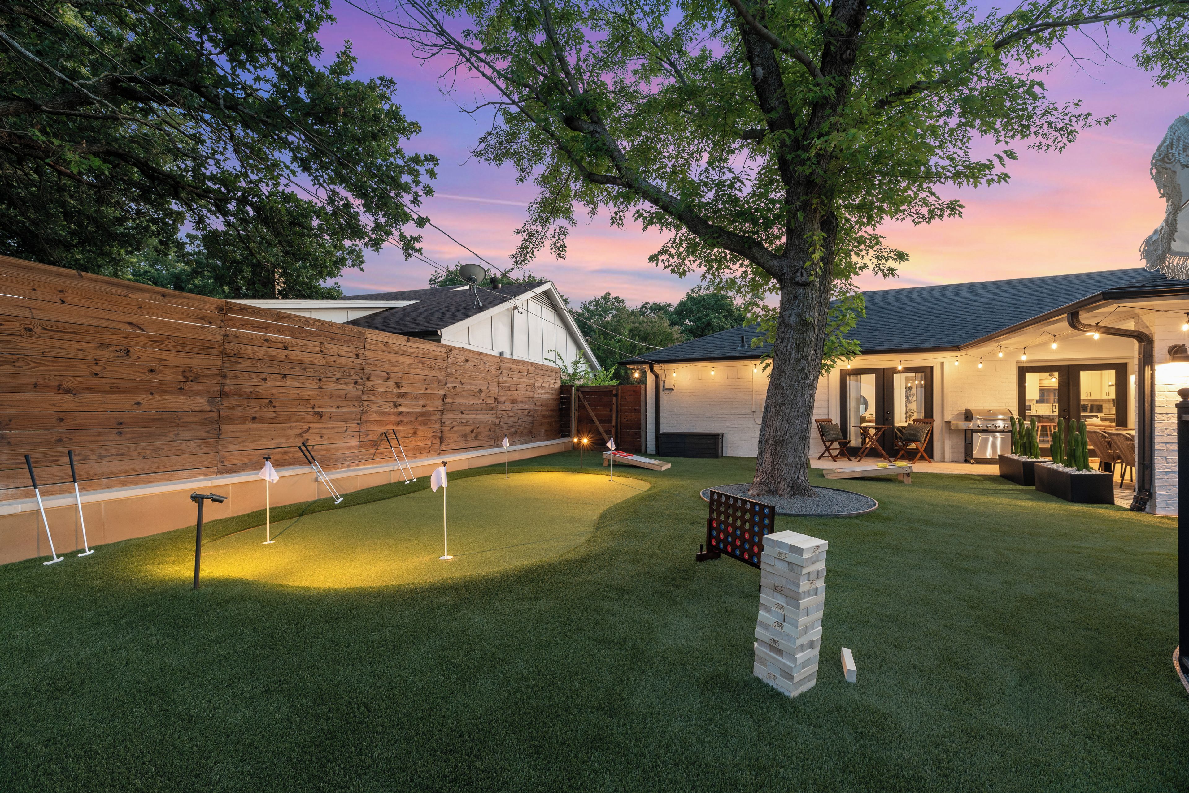 A backyard with a putting green, a wooden fence, and a tree.