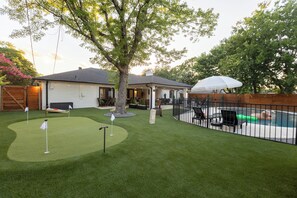 Ein Garten mit Pool, Kunstrasen und einer Terrassenfläche.