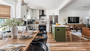 Eine moderne Küche mit weißen Schränken, einer zentralen Kochinsel und einem Essbereich mit Holztisch und Stühlen.