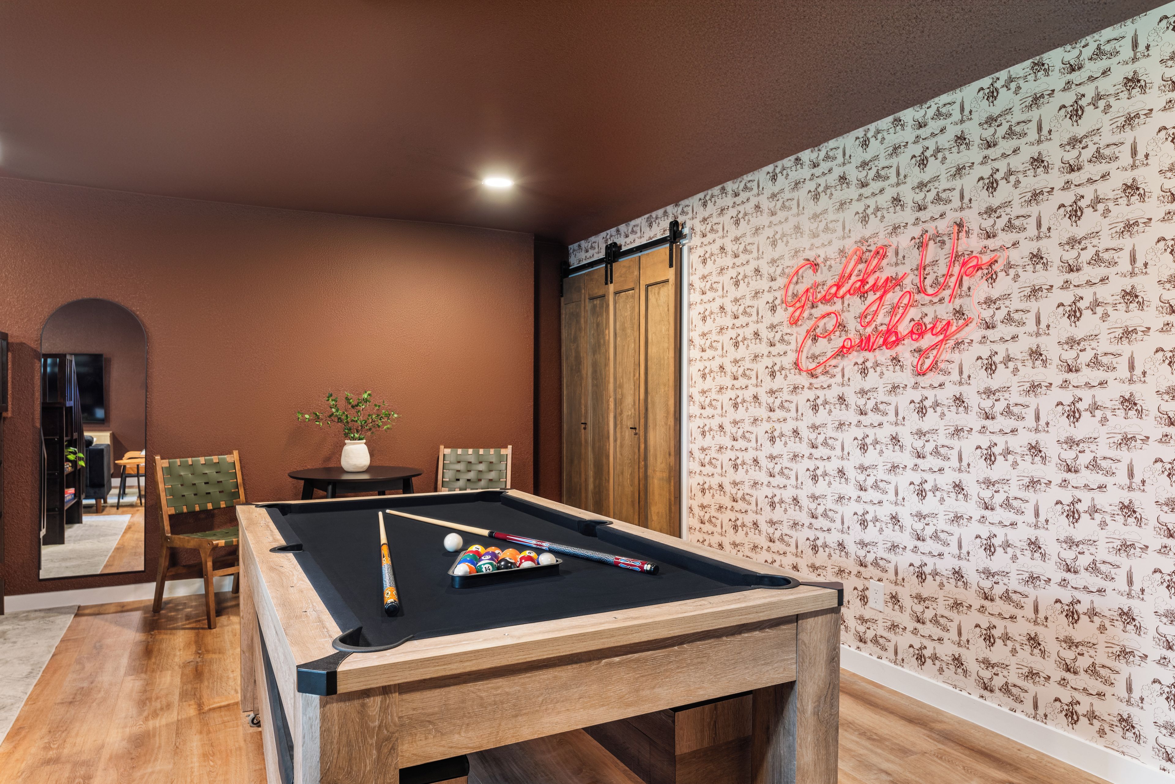 A pool table with balls, a chair, and a neon sign on the wall.