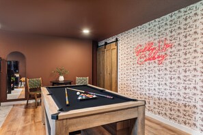 Une table de billard avec des billes, une chaise et un panneau lumineux au néon accroché au mur.