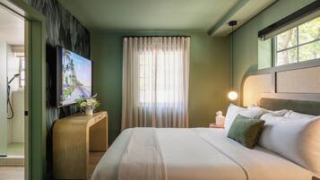 Ein Hotelzimmer mit Bett, Fernseher, einem Fenster mit Vorhängen und einem Nachttisch mit Lampe.
