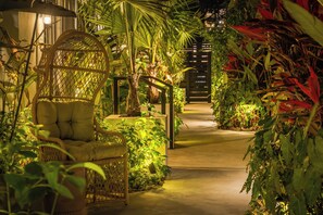 A pathway flanked by lush greenery and wicker furniture, leading to a wooden gate. - ART DECO MARELA BOUTIQUE (Miami Beach)