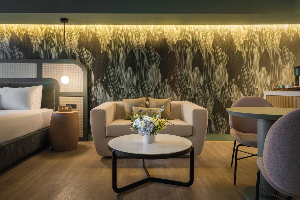 A modern hotel room with a bed, a sofa, a coffee table with flowers, and a wall with a textured design.
