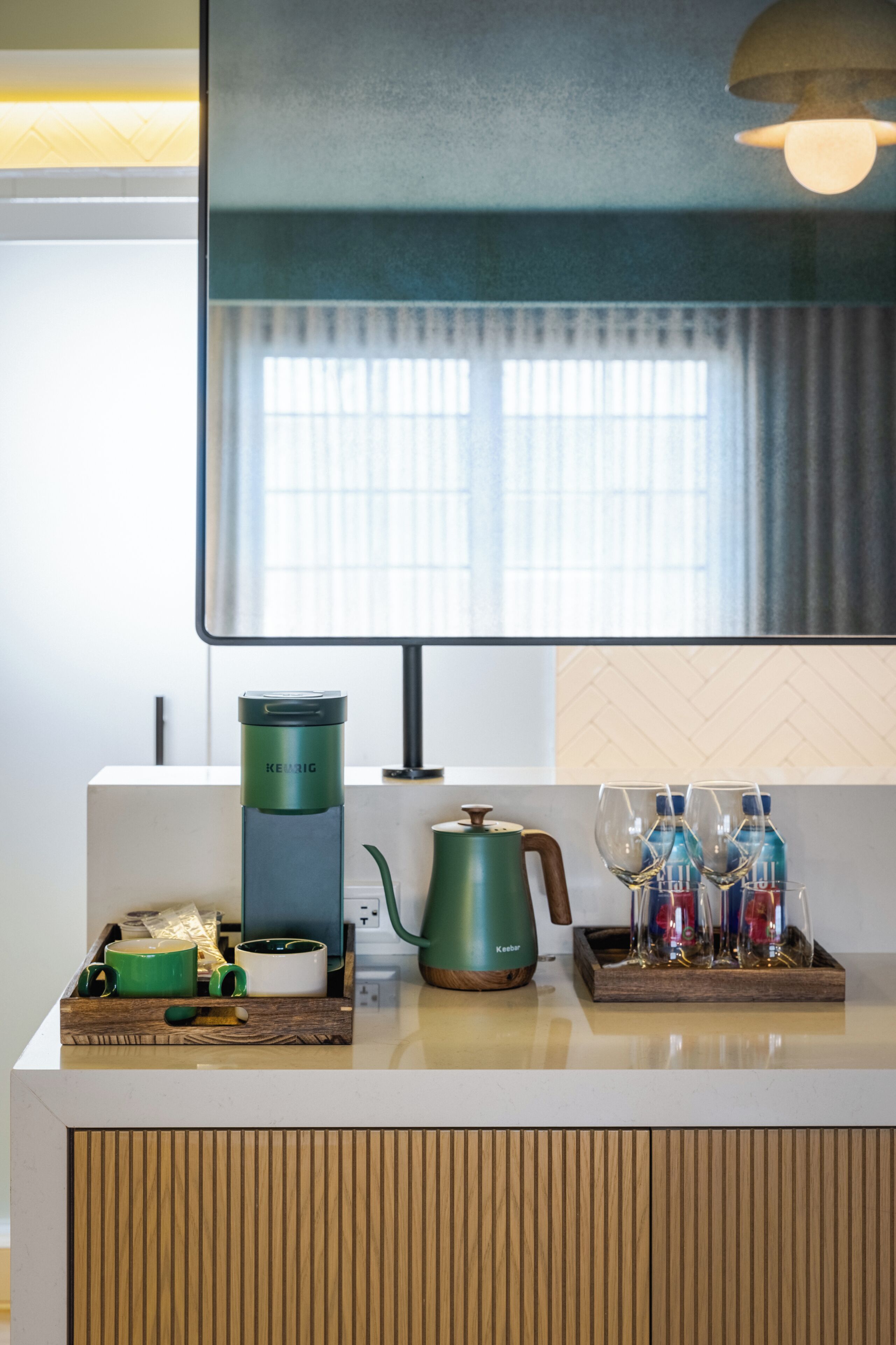 A modern kitchen with a coffee maker, kettle, and glassware on the counter.