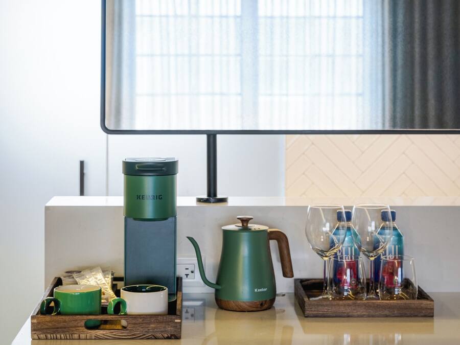 A modern kitchen with a coffee maker, kettle, and glassware on the counter.