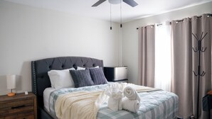 A neatly made bed with a checkered bedspread, a tufted headboard, and rolled towels. - Dual Master Rooms - Perfect for Groups & Family-friendly - Fire Pit, BBQ, Games (Moreno Valley)