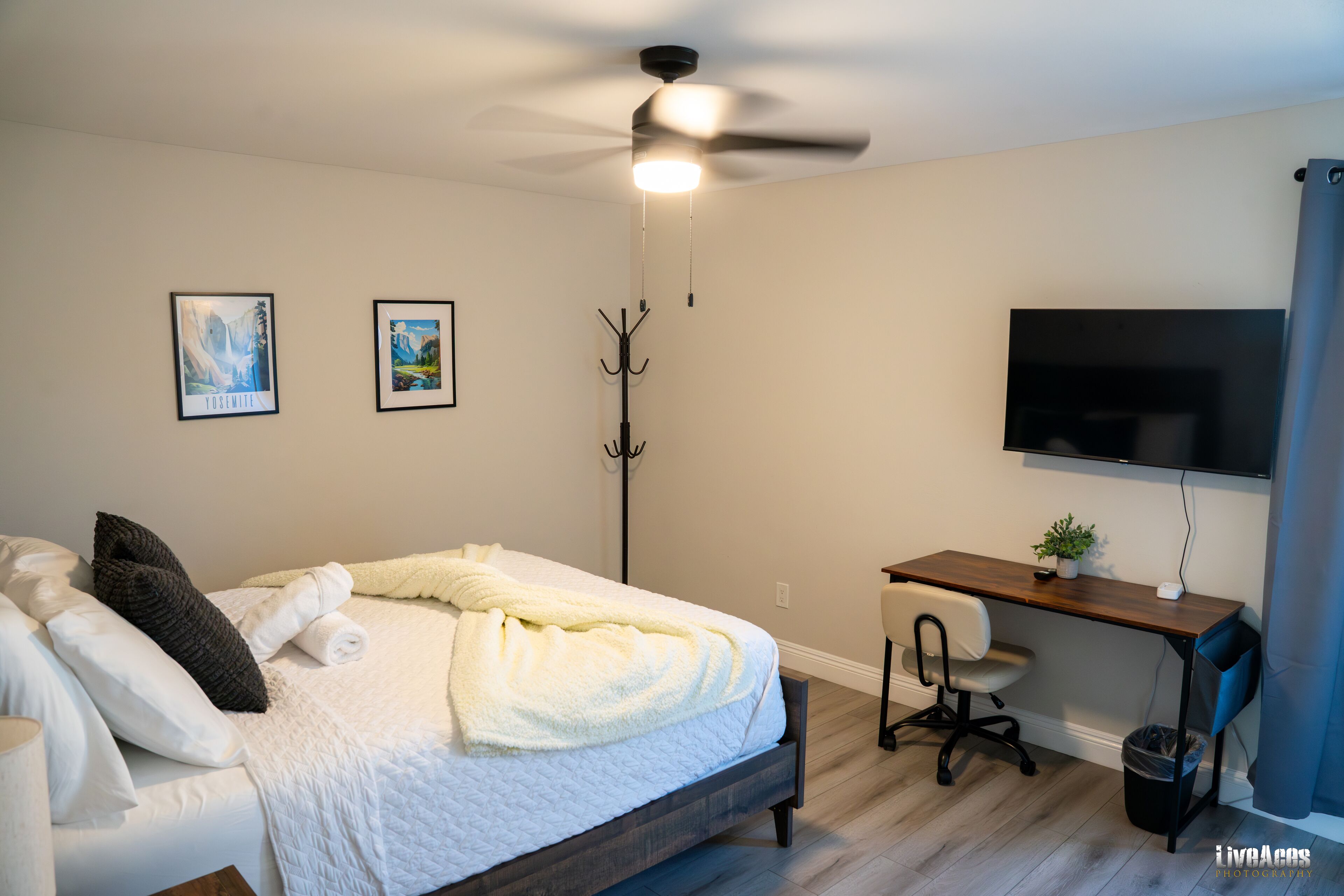 A bedroom with a bed, a desk, a chair, a coat rack, and a TV.