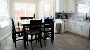 A modern kitchen with white cabinets, a dining table with chairs, and a coffee maker. - Dual Master Rooms - Perfect for Groups & Family-friendly - Fire Pit, BBQ, Games (Moreno Valley)