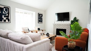 A modern living room with a sofa, armchair, and a fireplace. - Dual Master Rooms - Perfect for Groups & Family-friendly - Fire Pit, BBQ, Games (Moreno Valley)