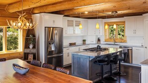 A modern kitchen with white cabinets, stainless steel appliances, a wooden dining table, and bar stools. - Enchanting Morrison Home with Views and Wifi (Morrison)