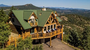 A log cabin with a green roof, wooden deck, and a scenic mountain backdrop. - Enchanting Morrison Home with Views and Wifi (Morrison)