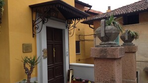 Un edificio amarillo con puerta marrón oscuro, un pilar de piedra con maceta y un pequeño jardín con caja de plantación de madera.