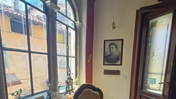 Una habitación con un sillón antiguo, un radiador, una mesa con una computadora portátil y una ventana con un cartel que dice 'RECEPTION'.