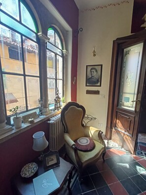 Habitació amb una butaca antiga, un radiador, una taula amb un ordinador portàtil i una finestra amb un rètol que diu 'RECEPTION'.